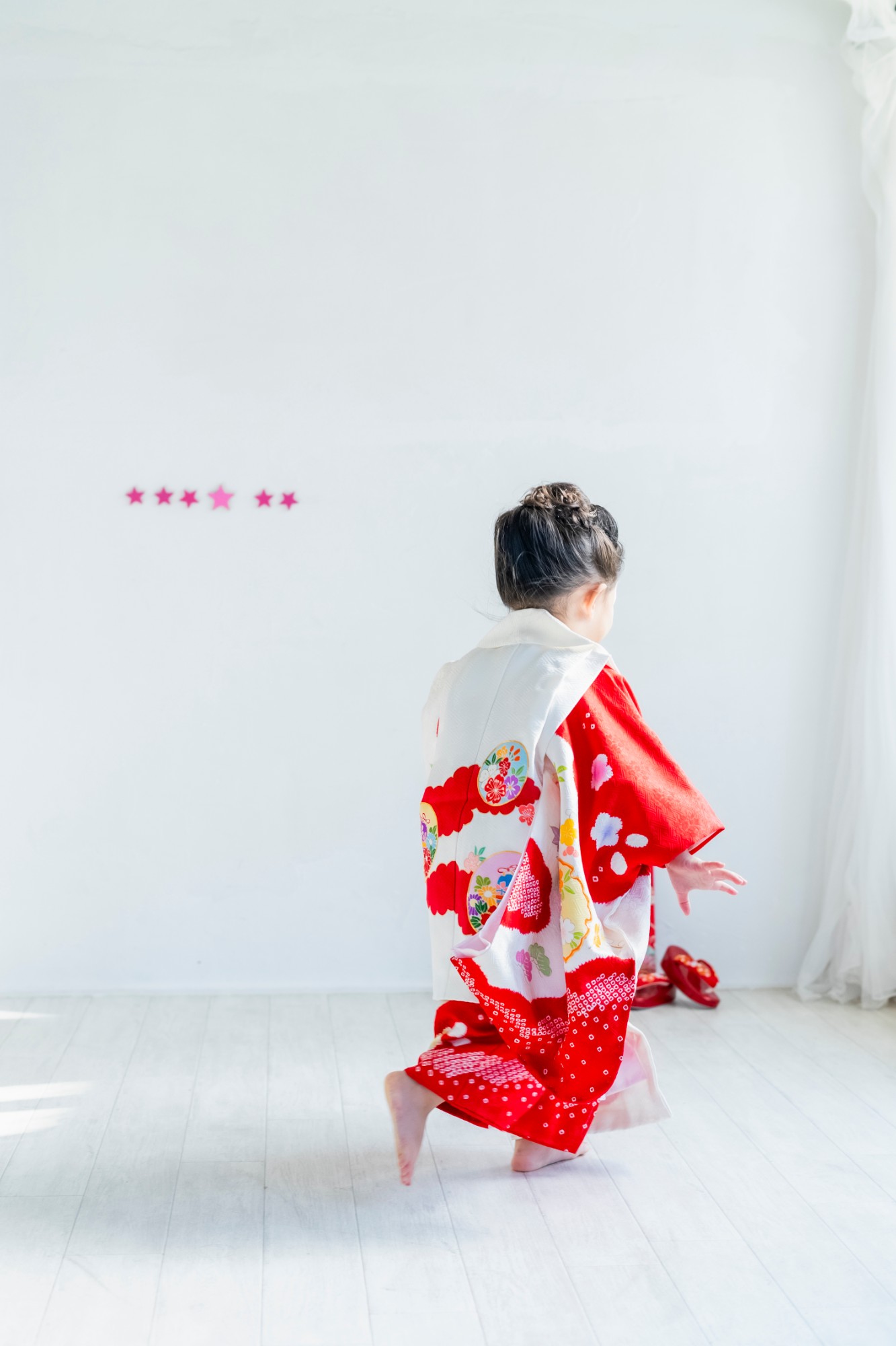 白い壁の前を、駆けていく赤い着物姿の女の子の後ろ姿