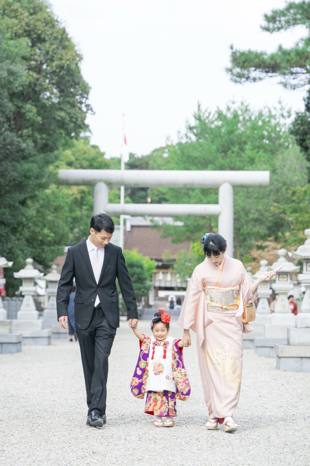 鳥居の前で手をつなぎ、笑顔で歩く七五三の家族
