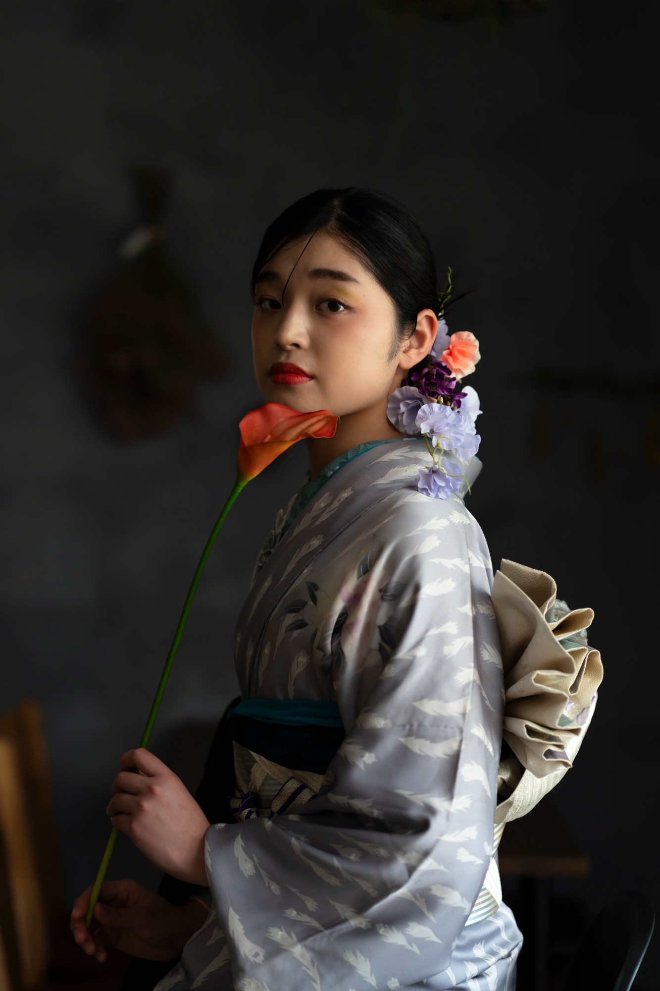 暗い背景の中で、赤いカラーの花を胸元に添えて振り向く振袖姿の女性