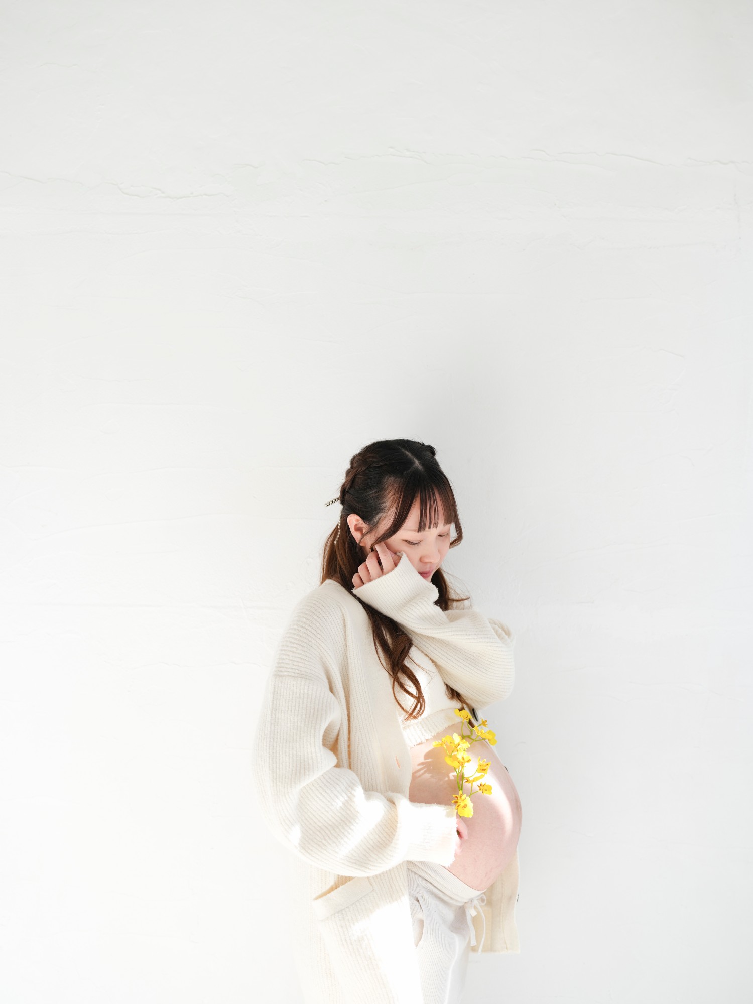 白い壁の前で、お腹に黄色い花を添える妊娠中の女性
