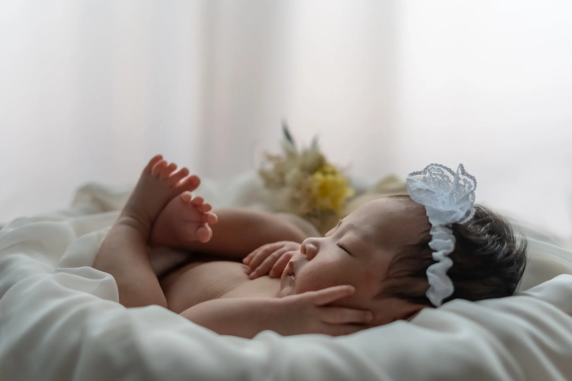 ドライフラワーのそばで眠る、レースのカチューシャをつけた新生児