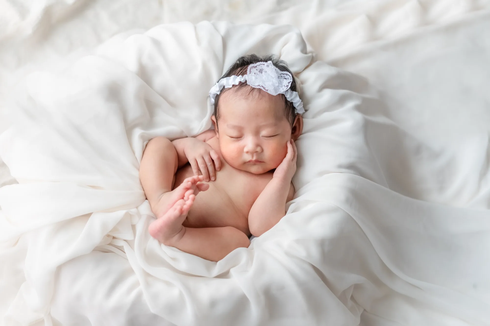 白いレースのカチューシャをつけ、籠の中で眠る新生児