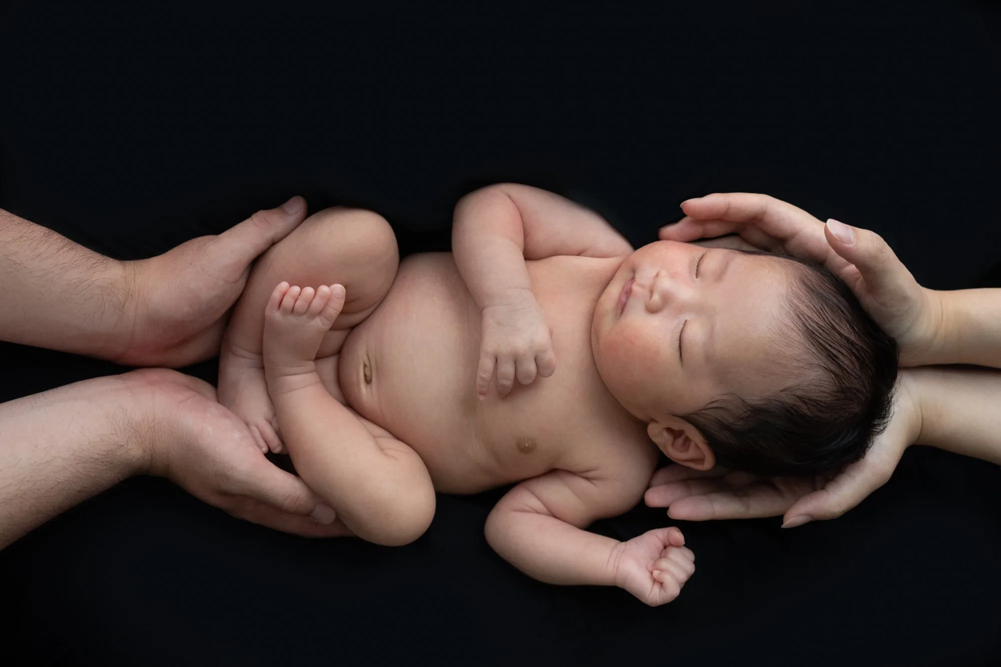 父親の腕の中で、指をくわえて眠る新生児(モノクロ)