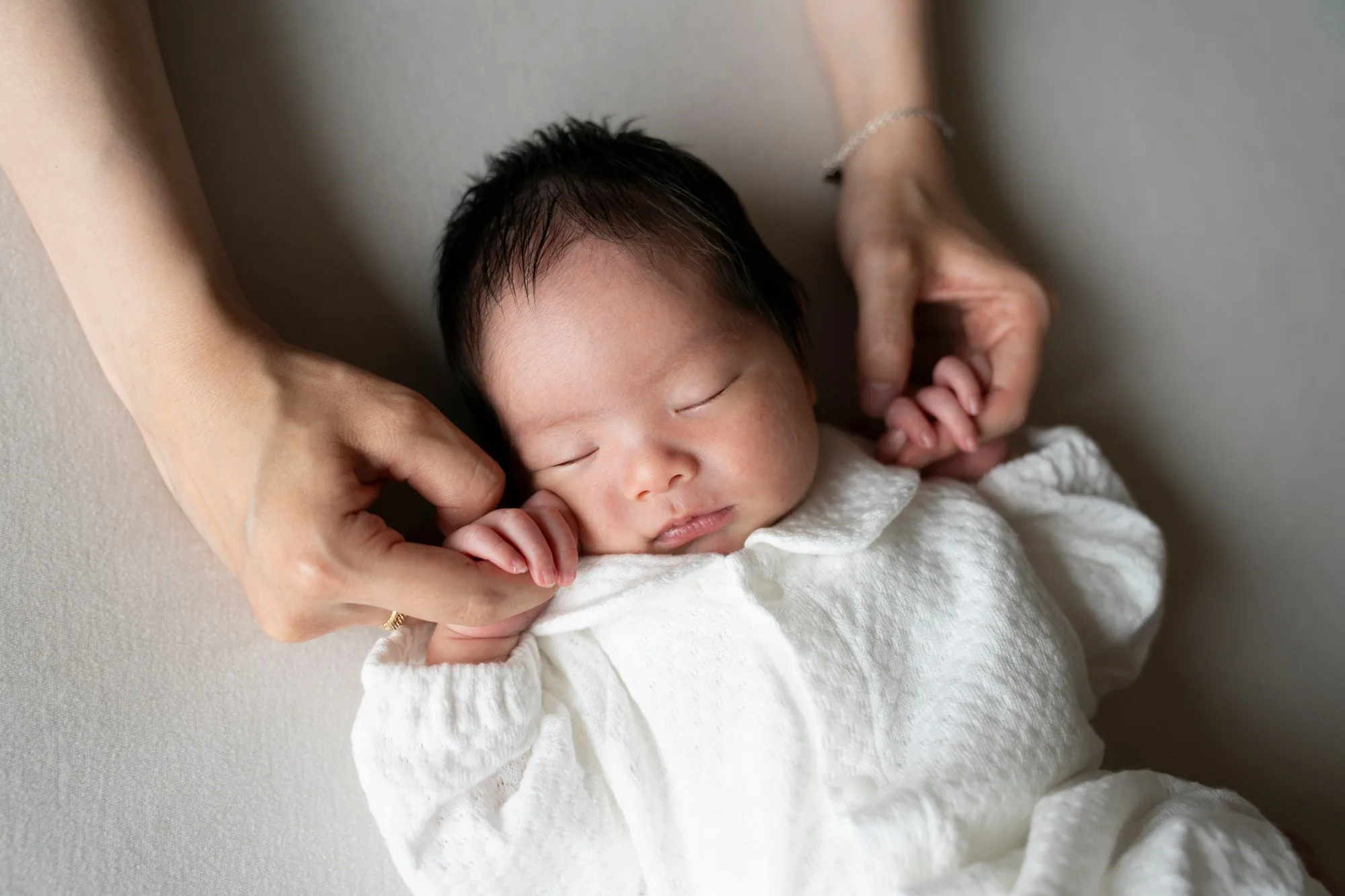 母親の手にそっと頭を預けて眠る新生児