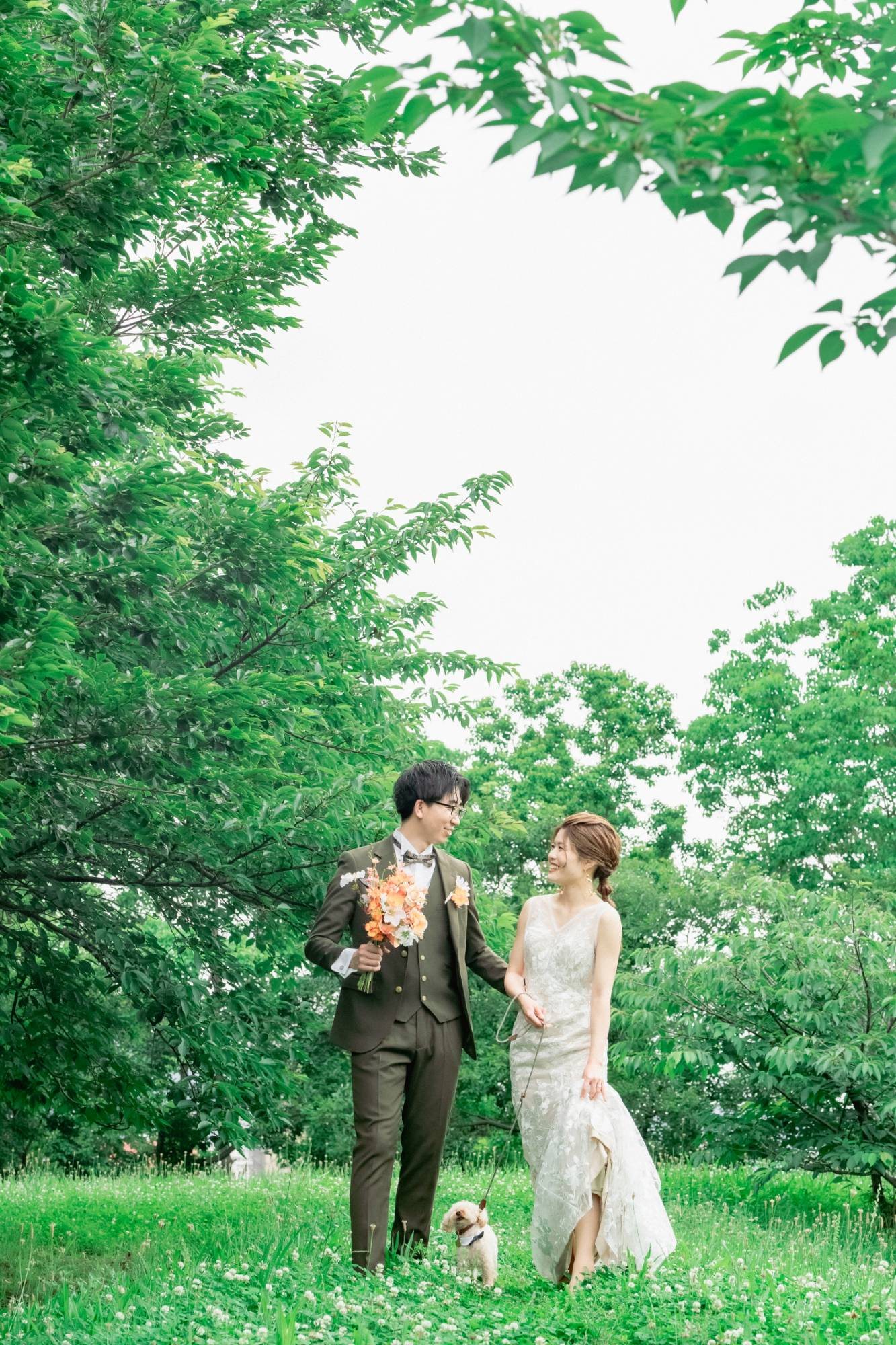 緑の芝生を、愛犬と一緒に歩く新郎新婦